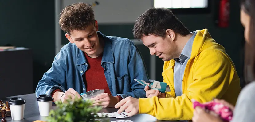 Young support worker playing cards with his support.